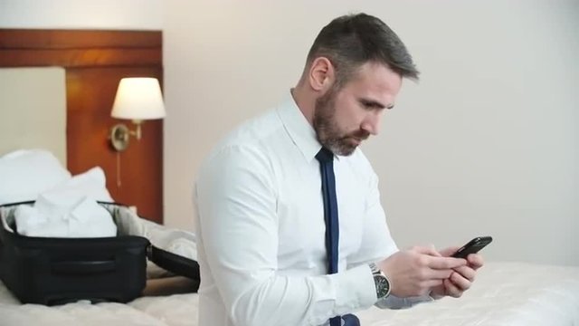 Businessman sitting in hotel room, making a call and talking on his phone