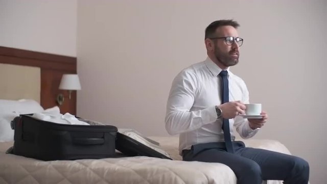 Businessman sitting in hotel room and drinking coffee on his bed