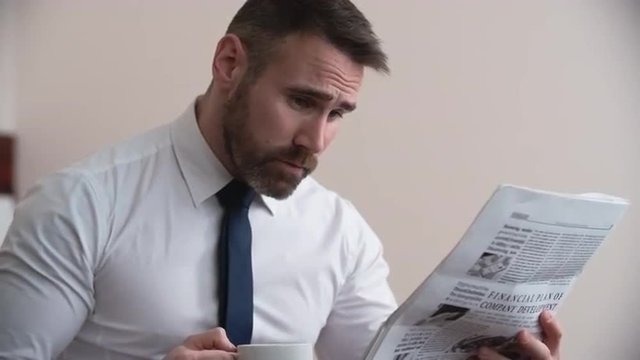 Close up of businessman drinking coffee and reading financial newspaper
