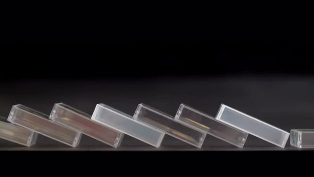 Slow motion clip of a row of plastic mini DV tape cases toppling like dominos.  Locked-off shot with black background, originally recorded in 4K at 60fps.