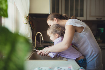 Daughter with her mother to wash their hands in the kitchen sink - Powered by Adobe