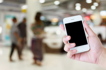 hands holding mobile phone with new cars in showroom