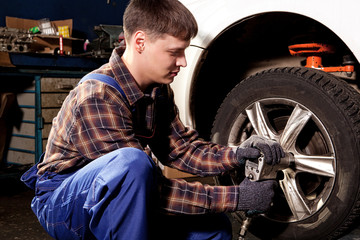 Car mechanic screwing or unscrewing car wheel of lifted automobi