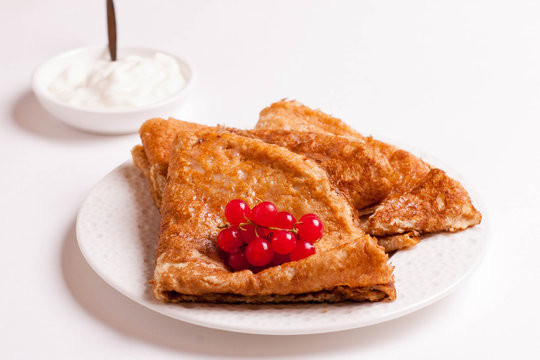 crepes with red currants and sour cream on a plate isolated