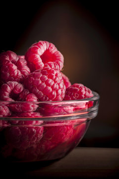 Raspberries close up in glass jar on wooden table and dark background in studio