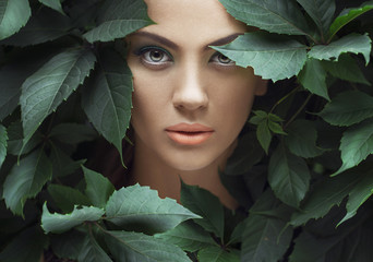 Sexy Beauty Girl with coral Lips. Provocative green Make up. Luxury Woman with Green Eyes. Fashion Brunette Portrait in wild leaves (grapes),  natural background. Gorgeous Woman Face. Long Hair