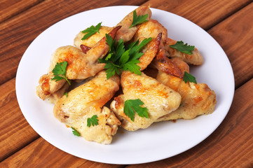 Plate with baked chicken wings and parsley on a wooden background