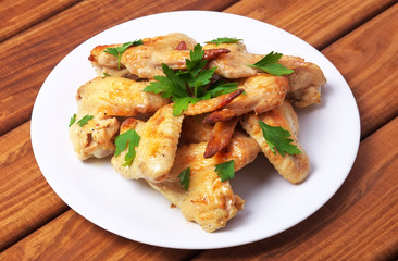 Plate with baked chicken wings and parsley on a wooden background