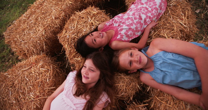 Little girls lying on straw in circle with heads together 