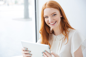Fototapeta premium Happy woman laughing and using tablet in cafe