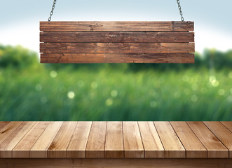 Wood table with hanging wooden sign on green leaves background