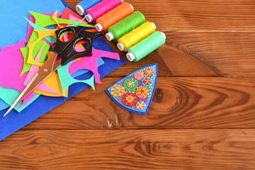 Obraz premium Handmade brooch from felt scrap, frugal craft. Thread, needle, scissors. Wooden background with copy space for text 