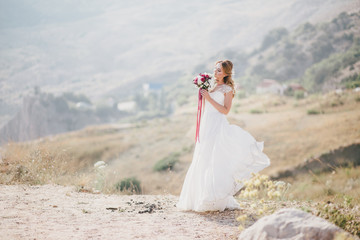 Fototapeta na wymiar Beautiful young happy bride standing on the top of the mountain