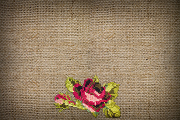 horizontal background of coarse burlap embroidered cross-stitch rose closeup