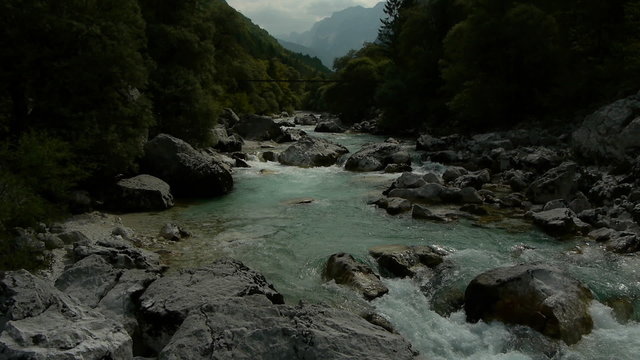 Close aerial flight of the upstream river Soca with suspension bridge at background in the mountain valley.
