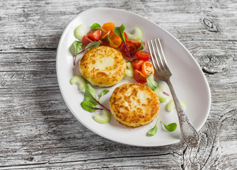 Potato patties and fresh tomato and celery salad on a light ceramic plate on  wooden background.