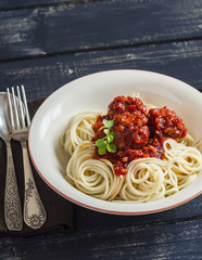 Spaghetti and meatballs in tomato sauce in a ceramic saucer on dark wooden background. Delicious food