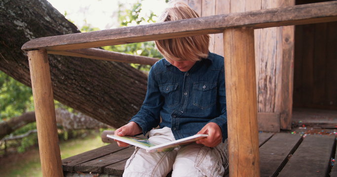 Boy sitting in treehouse reading a childrens book
