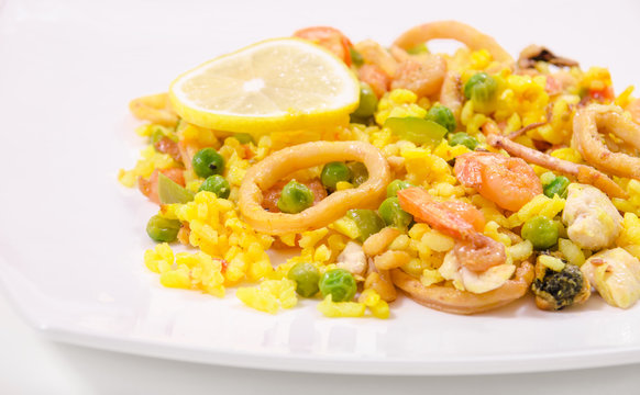 Paella with chicken and seafood on a white plate, close-up, side view
