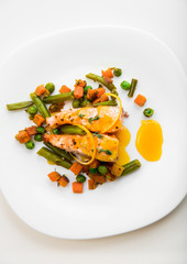 Baked salmon with green beans, carrots, green peas, thyme and orange sauce on a white plate, top view