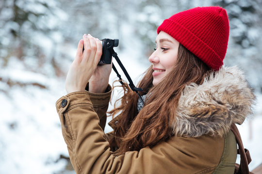 Smiling woman walking and taking pictures in winter forest