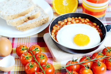 Fried egg with beans, toast bread, fresh juice, tomatoes and oranges