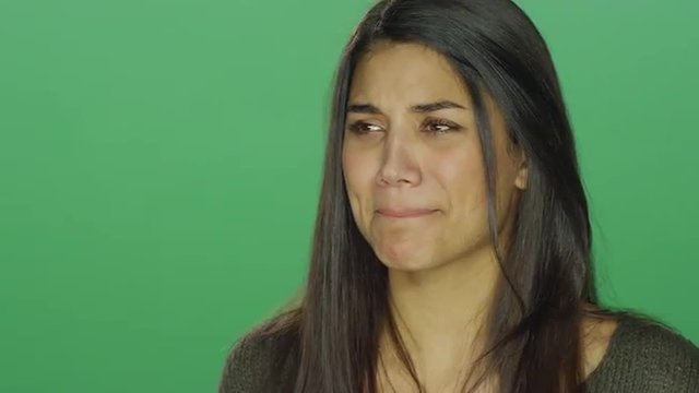 Young woman starting to cry, on a green screen studio background