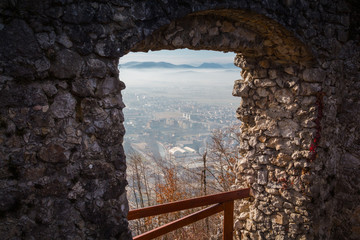 View of town part, covered with morning mist, through a passage in the wall of ruined Old Castle on the mountain top, Kamnik, Slovenia.