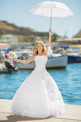Fototapeta na wymiar Beautiful bride in wedding dress with white umbrella posing over