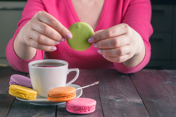 Female hand with tasty colorful macaroons on dark wooden backgro