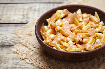 Poutine Canadian homemade traditional fast food meal with fries, curd cheese, gravy and beer on vintage wooden table background. Rustic style,
