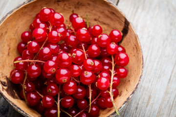 Redcurrant on a branch close to a wooden bowl.