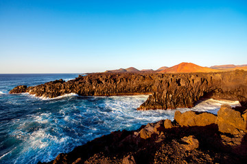 Los Hervideros rocky coast with wavy ocean and volcanos on the background on the sunset on Lanzarote island in Spain