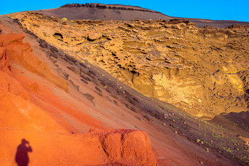 Red volcanic rocks with tourist shadow in El Golfo bay on Lanzarote island in Spain