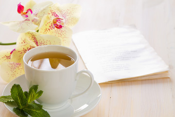 A cup of green tea with yellow blotchy orchid flowers and fresh mint