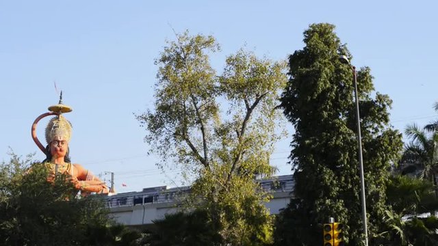 Locked-on shot of metro train moving in front of giant statue of lord Hanuman, Karol Bagh, New Delhi, India 