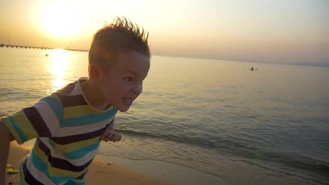 Slow motion of a boy in striped t-shirts and mohawk on the head getting angry and making furious face before run at the seaside at sunset