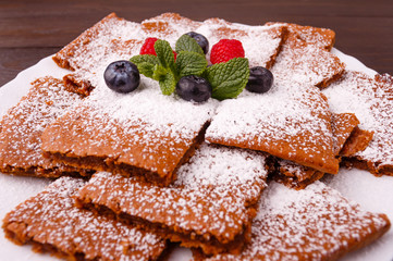 Honeyed cake with ginger dusted with icing sugar with raspberry, bilberry, mint on  plate on wooden background