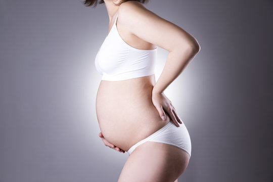 Caucasian pregnant woman in white lingerie with back pain on gray studio background