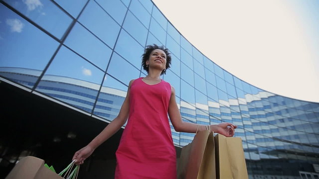 African american woman with shopping bags walking in a city at sunset. Slow motion