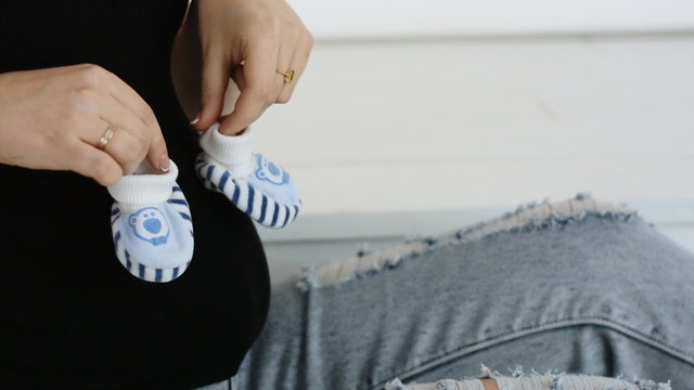 Young pregnant woman playing with booties. Booties on the belly. Slow motion. Close-up