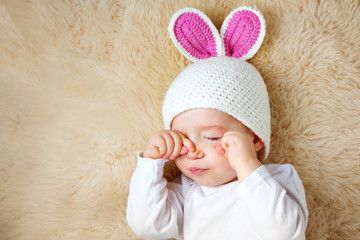 one year old baby lying in bunny hat on lamb wool
