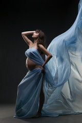 Fototapeta premium Young beauty and sexy caucasian pregnant woman with blue silk on gray studio background