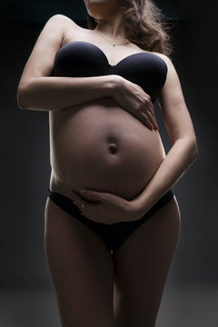 Young beauty and sexy caucasian pregnant woman in black lingerie on gray studio background