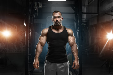 Fototapeta na wymiar A strong muscular relief tanned handsome man on a gym background.