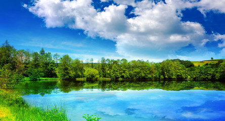 Fototapeta na wymiar Lake and green trees on sky background.