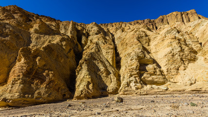 High sandstone cliffs painted in many glowing shades of orange, gold and red. Narrow canyon with vertical walls on both sides. Rocky landscape background. Golden canyon, Death Valley