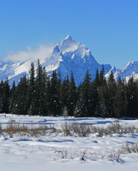 Snow mist blowing off Grand Tetons peaks  in front of snowfield