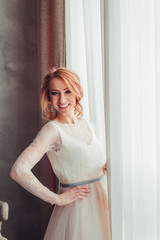 Fototapeta premium Beautiful bride is standing at the window with bunch of flowers.