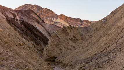 The gorge cuts into brightly colored sandstone rocks. Narrow canyon with vertical walls on both sides. Rocky landscape background. Sandstone formations in Golden canyon, Death Valley